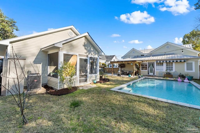 rear view of house featuring a yard, a sunroom, an outdoor pool, central AC unit, and a patio area