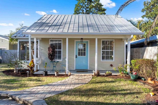 bungalow-style house with a front lawn, fence, a porch, metal roof, and a standing seam roof