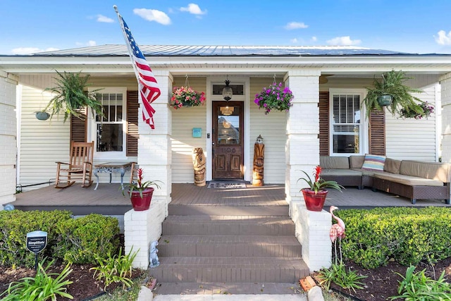 view of exterior entry with a porch, brick siding, and metal roof