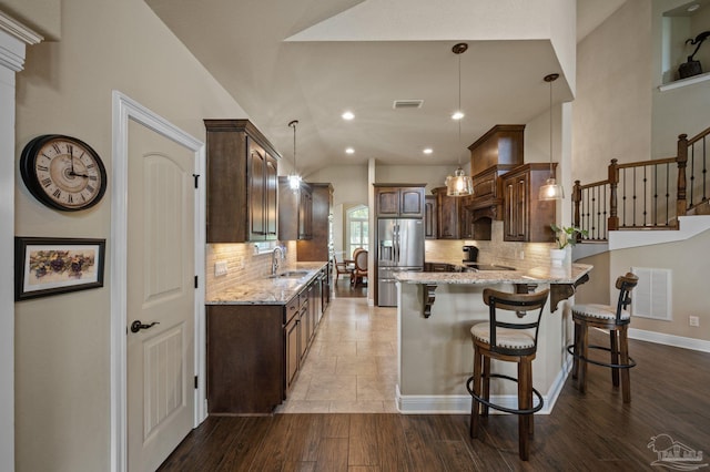 kitchen with a sink, visible vents, dark brown cabinets, a peninsula, and stainless steel fridge