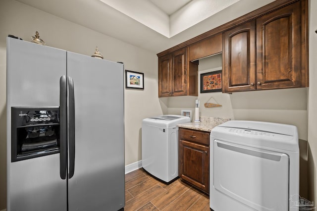 clothes washing area with wood finished floors, washing machine and clothes dryer, cabinet space, and baseboards