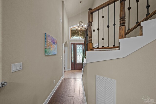 doorway to outside featuring an inviting chandelier, visible vents, baseboards, a towering ceiling, and wood finished floors