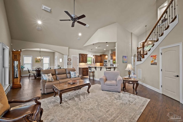 living area featuring arched walkways, ceiling fan with notable chandelier, dark wood-style flooring, visible vents, and high vaulted ceiling