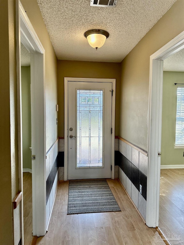 doorway featuring light wood-type flooring, visible vents, plenty of natural light, and a textured ceiling