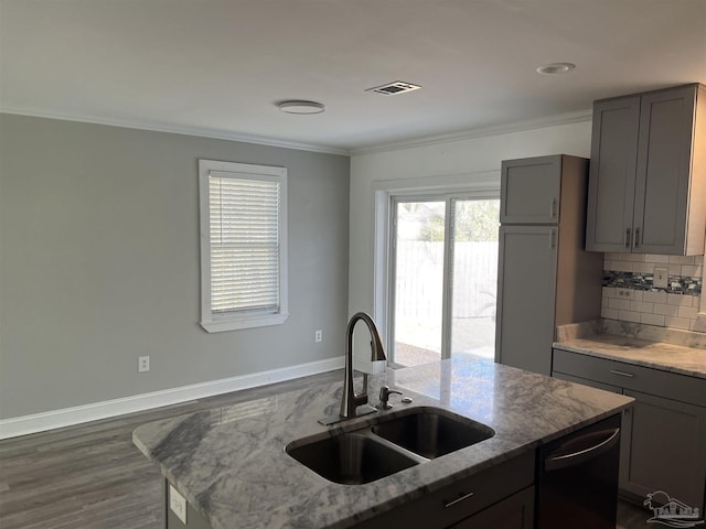 kitchen with sink, dishwasher, backsplash, light stone counters, and an island with sink