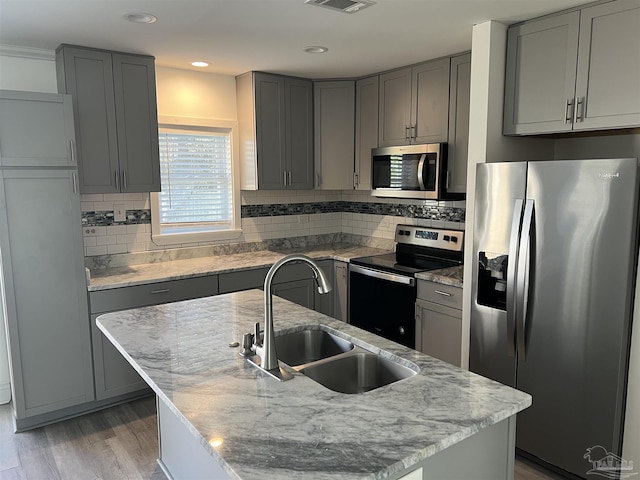 kitchen featuring sink, a kitchen island with sink, stainless steel appliances, light hardwood / wood-style floors, and light stone countertops