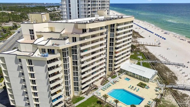 view of building exterior featuring a water view, a community pool, and a view of the beach