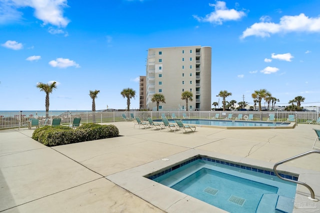 view of swimming pool with a hot tub, a water view, and a patio area