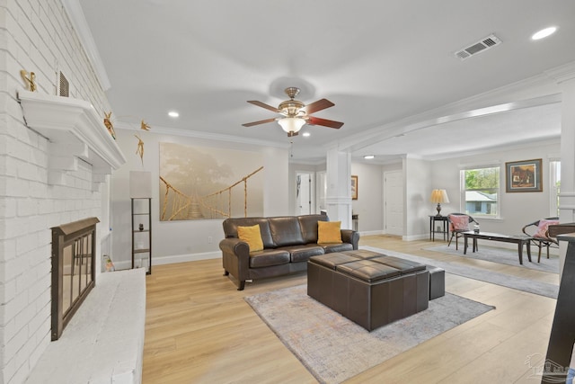 living room with light wood finished floors, a brick fireplace, visible vents, a ceiling fan, and crown molding
