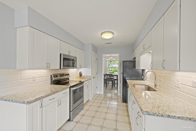 kitchen featuring a sink, decorative backsplash, light stone counters, white cabinets, and appliances with stainless steel finishes
