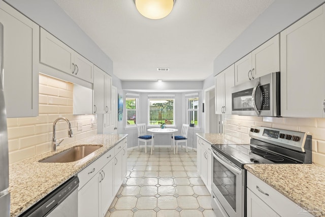 kitchen featuring a sink, decorative backsplash, white cabinetry, baseboards, and appliances with stainless steel finishes