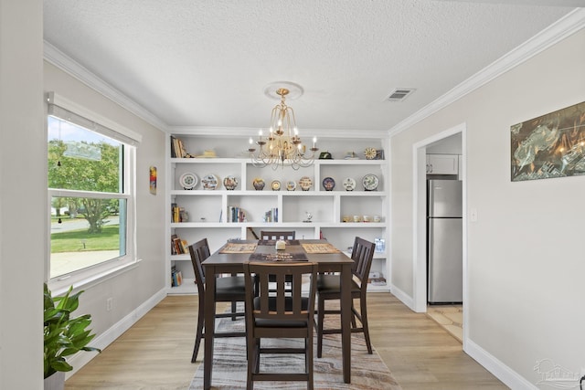 dining area featuring light wood-type flooring, visible vents, an inviting chandelier, and a textured ceiling