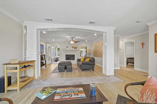 living area featuring visible vents, ornate columns, light wood finished floors, and a brick fireplace