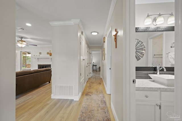hall with crown molding, light wood finished floors, a sink, and visible vents