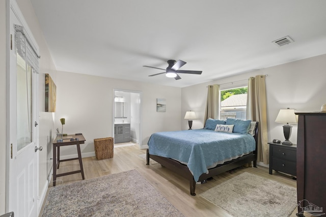 bedroom featuring light wood finished floors, ceiling fan, ensuite bath, visible vents, and baseboards