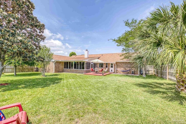 back of house with brick siding, a yard, a fenced backyard, a chimney, and a deck