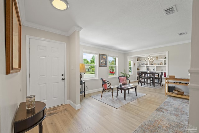foyer featuring visible vents, an inviting chandelier, crown molding, and light wood finished floors