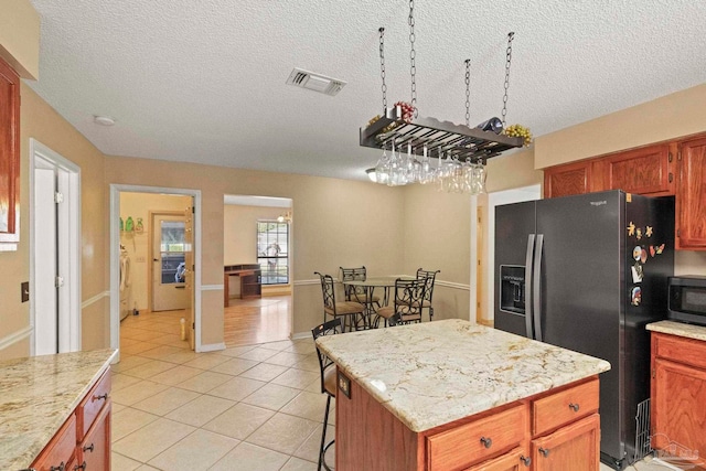 kitchen featuring light stone counters, a textured ceiling, stainless steel appliances, a center island, and light tile patterned flooring