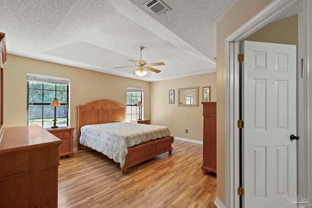 bedroom featuring ceiling fan, a raised ceiling, light wood-type flooring, and a textured ceiling