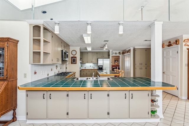 kitchen with tile countertops, a sink, appliances with stainless steel finishes, decorative backsplash, and open shelves