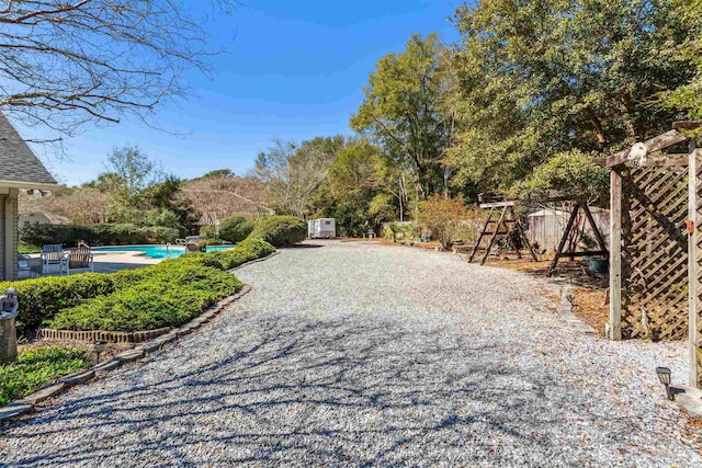 view of yard featuring an outdoor pool, an outbuilding, gravel driveway, fence, and a storage unit