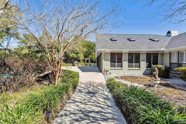 exterior space with a patio area, brick siding, and roof with shingles