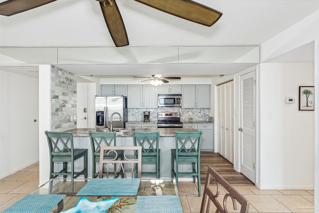 kitchen with ceiling fan, gray cabinets, appliances with stainless steel finishes, a kitchen bar, and decorative backsplash