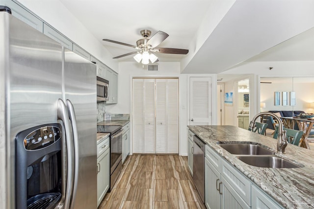 kitchen with appliances with stainless steel finishes, gray cabinetry, light wood-type flooring, ceiling fan, and sink