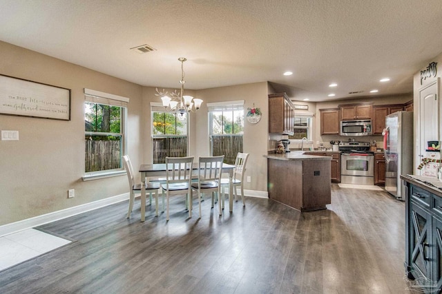 dining area with sink, dark wood-type flooring, a textured ceiling, and a notable chandelier