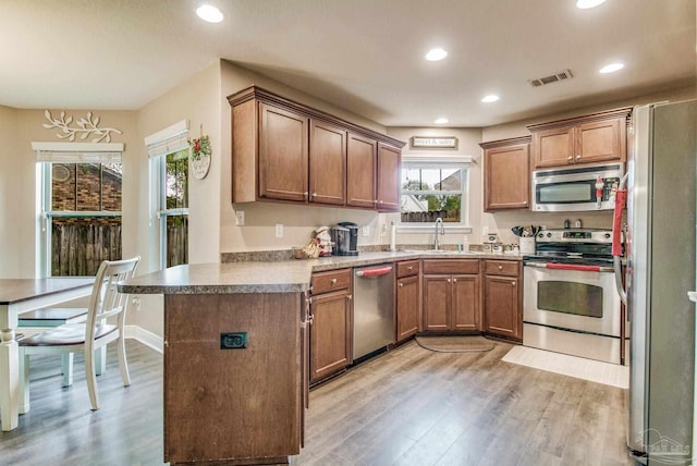 kitchen with kitchen peninsula, sink, appliances with stainless steel finishes, and light hardwood / wood-style flooring