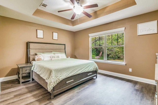 bedroom featuring hardwood / wood-style flooring, ceiling fan, and a raised ceiling