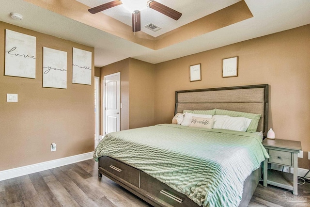 bedroom with a raised ceiling, ceiling fan, and wood-type flooring