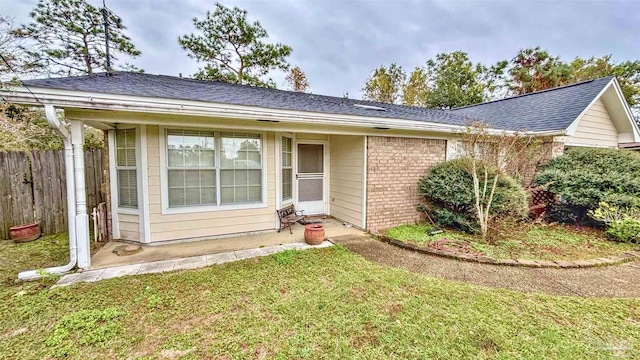 view of front of property with roof with shingles, fence, a front lawn, and brick siding