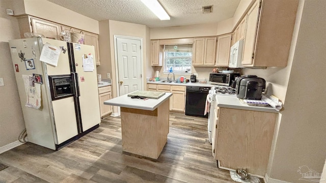 kitchen with light brown cabinetry, white appliances, a center island, and a textured ceiling