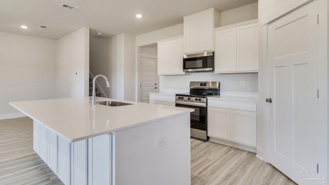 2733 Chevy Cir, Pace, FL 32571 - kitchen with stainless steel appliances, a sink, light wood-style floors, an island with sink, and white cabinets