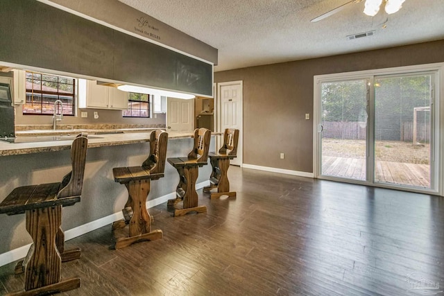 kitchen with a healthy amount of sunlight, dark hardwood / wood-style floors, white cabinets, and a kitchen breakfast bar