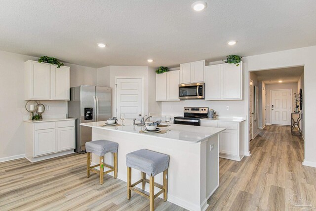 kitchen with light hardwood / wood-style floors, appliances with stainless steel finishes, white cabinetry, and a kitchen island with sink