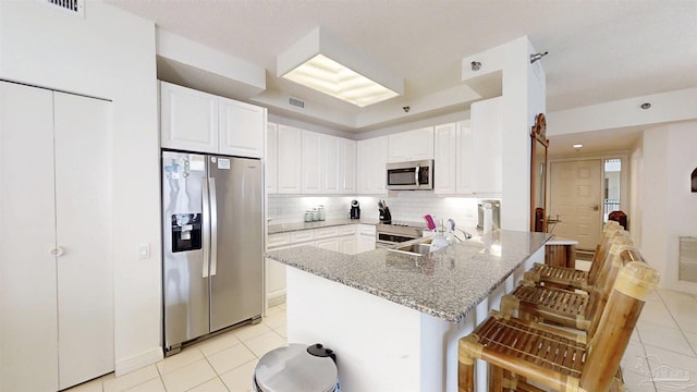 kitchen with white cabinetry, a kitchen bar, light stone counters, kitchen peninsula, and stainless steel appliances