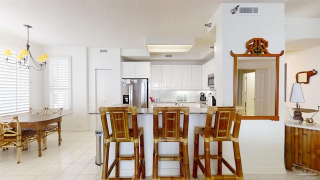 kitchen featuring a kitchen bar, hanging light fixtures, white cabinets, and appliances with stainless steel finishes