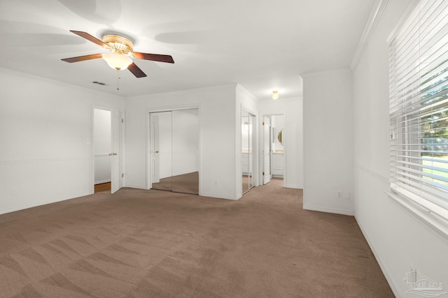 unfurnished bedroom with carpet flooring, ceiling fan, ornamental molding, and two closets