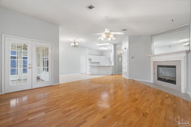 unfurnished living room featuring light hardwood / wood-style flooring, a fireplace, a textured ceiling, ceiling fan with notable chandelier, and french doors