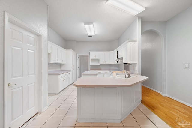 kitchen with light tile patterned floors, sink, kitchen peninsula, and white cabinets