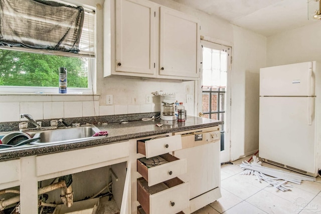 kitchen with light tile patterned floors, a sink, freestanding refrigerator, and white cabinetry