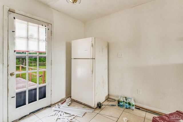 interior space with light tile patterned floors, baseboards, and freestanding refrigerator