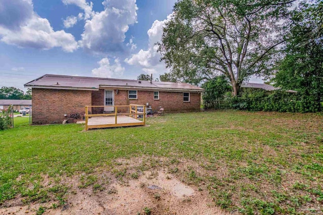 rear view of property with brick siding, a yard, a wooden deck, and fence