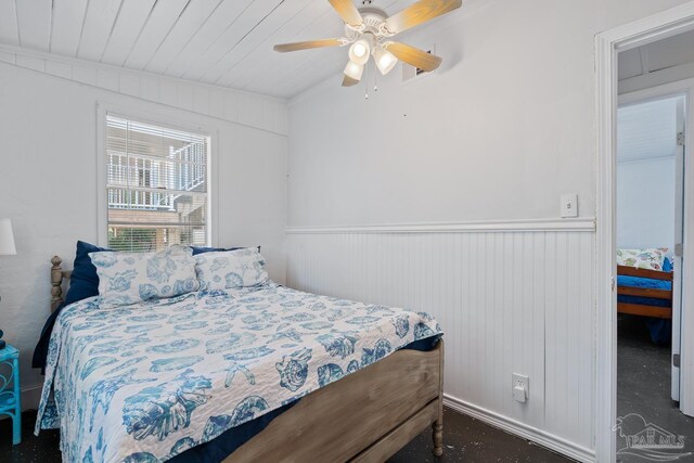 bedroom with ceiling fan, wood ceiling, and a wainscoted wall