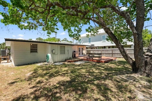 rear view of house with french doors, a deck, central air condition unit, fence, and a yard