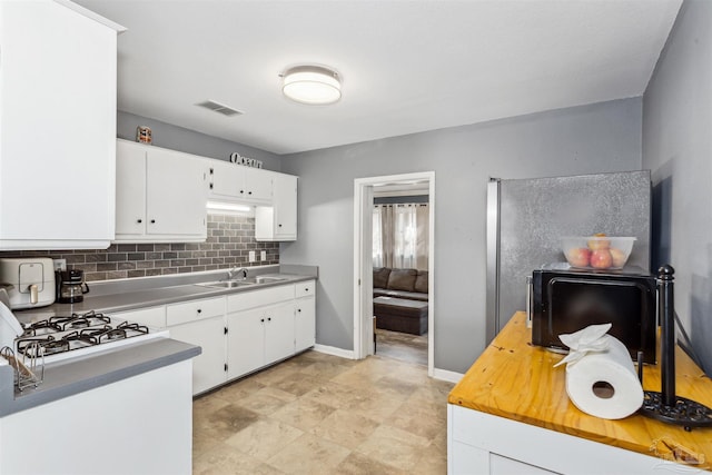 kitchen with tasteful backsplash, sink, white cabinets, and white gas cooktop