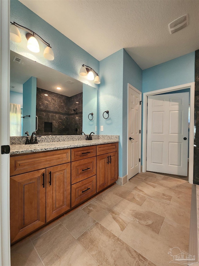 bathroom with a textured ceiling, vanity, and tiled shower