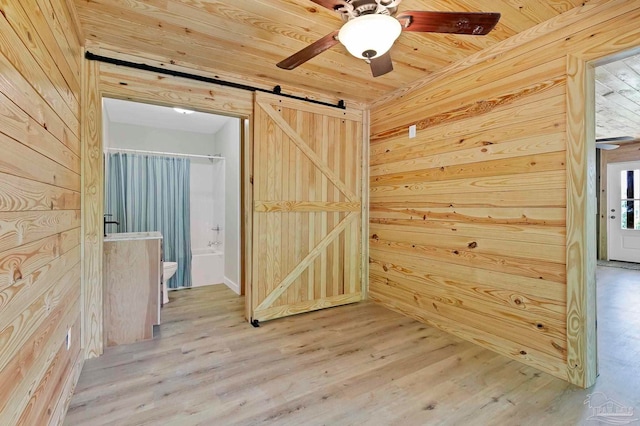 unfurnished room with light wood-style floors, wood ceiling, ceiling fan, a barn door, and wooden walls